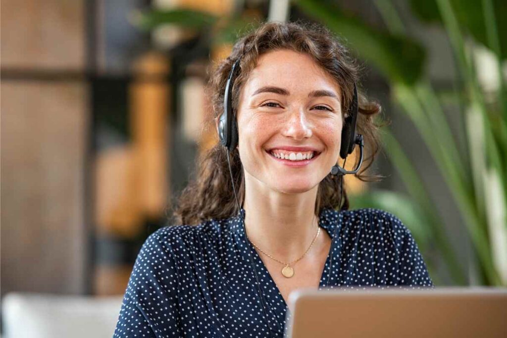 Glimlachende vrouw met headset die achter een laptop werkt